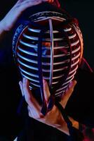 Close up shot, Kendo fighter wearing in an armor and traditional kimono is tying the lacing on his helmet standing against a black background. photo