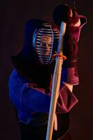 Close up shot, Kendo fighter wearing in an armor, traditional kimono, helmet practicing martial art with shinai bamboo sword, black background. photo