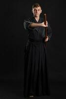 kendo gurú vistiendo en un tradicional japonés kimono es practicando marcial Arte con el shinai bambú espada en contra un negro estudio antecedentes. foto