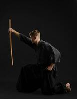 Kendo guru wearing in a traditional japanese kimono is practicing martial art with the shinai bamboo sword against a black studio background. photo