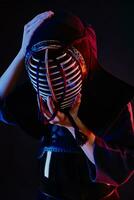 Close up shot, Kendo fighter wearing in an armor and traditional kimono is tying the lacing on his helmet standing against a black background. photo