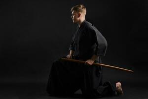 kendo gurú vistiendo en un tradicional japonés kimono es practicando marcial Arte con el shinai bambú espada en contra un negro estudio antecedentes. foto