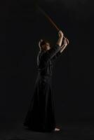 Kendo guru wearing in a traditional japanese kimono is practicing martial art with the shinai bamboo sword against a black studio background. photo