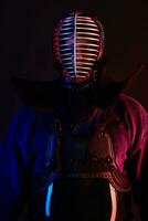 Close up shot, Kendo fighter wearing in an armor, traditional kimono, helmet practicing martial art with shinai bamboo sword, black background. photo