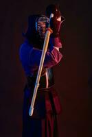 Close up shot, Kendo fighter wearing in an armor, traditional kimono, helmet practicing martial art with shinai bamboo sword, black background. photo