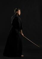 Kendo guru wearing in a traditional japanese kimono is practicing martial art with the shinai bamboo sword against a black studio background. photo