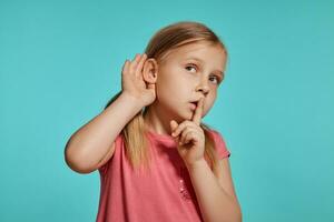 Close-up shot of beautiful blonde little girl in a pink dress posing against a blue background. photo