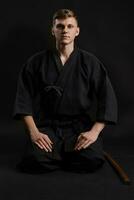 Kendo guru wearing in a traditional japanese kimono is practicing martial art with the shinai bamboo sword against a black studio background. photo