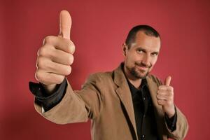 Middle-aged man with beard and mustache, wears black shirt and brown jacket posing against a red background. Sincere emotions concept. photo