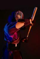 Close up shot, Kendo fighter wearing in an armor, traditional kimono, helmet practicing martial art with shinai bamboo sword, black background. photo