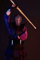 cerca arriba disparo, kendo combatiente vistiendo en un armadura, tradicional kimono, casco practicando marcial Arte con shinai bambú espada, negro antecedentes. foto