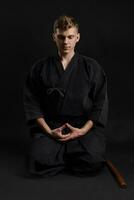 Kendo guru wearing in a traditional japanese kimono is practicing martial art with the shinai bamboo sword against a black studio background. photo