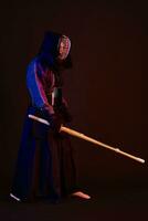 Close up shot, Kendo fighter wearing in an armor, traditional kimono, helmet practicing martial art with shinai bamboo sword, black background. photo