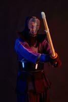 Close up shot, Kendo fighter wearing in an armor, traditional kimono, helmet practicing martial art with shinai bamboo sword, black background. photo