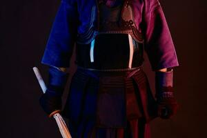 cerca arriba disparo, kendo combatiente vistiendo en un armadura, tradicional kimono es practicando marcial Arte con shinai bambú espada, negro antecedentes. foto