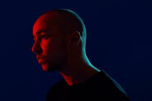 Studio shot of a young tattoed bald man posing against a blue background. 90s style. photo