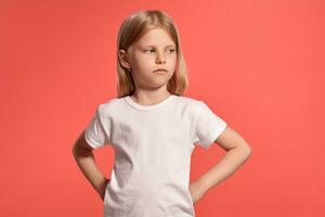 de cerca estudio Disparo de un bonito rubia pequeño niña en un blanco camiseta posando en contra un rosado antecedentes. foto