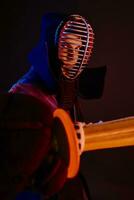 Close up shot, Kendo fighter wearing in an armor, traditional kimono, helmet practicing martial art with shinai bamboo sword, black background. photo