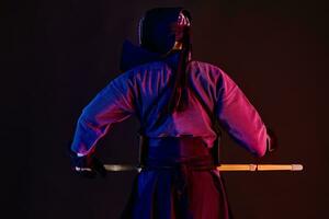 cerca arriba. kendo combatiente vistiendo en un armadura, tradicional kimono, casco practicando marcial arte, shinai bambú espada, en pie atrás, negro antecedentes. foto