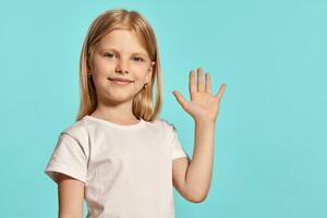 de cerca estudio Disparo de un encantador rubia pequeño niña en un blanco camiseta posando en contra un azul antecedentes. foto