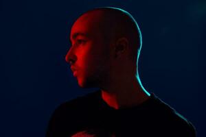 Studio shot of a young tattoed bald man posing against a blue background. 90s style. photo