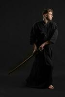 kendo gurú vistiendo en un tradicional japonés kimono es practicando marcial Arte con el shinai bambú espada en contra un negro estudio antecedentes. foto