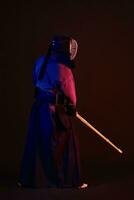 Close up shot, Kendo fighter wearing in an armor, traditional kimono, helmet practicing martial art with shinai bamboo sword, black background. photo