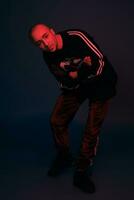 Studio shot of a young tattoed bald man posing against a dark blue background. 90s style. photo