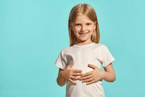 Close-up studio shot of a lovely blonde little girl in a white t-shirt posing against a blue background. photo