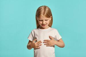 Close-up studio shot of a lovely blonde little girl in a white t-shirt posing against a blue background. photo