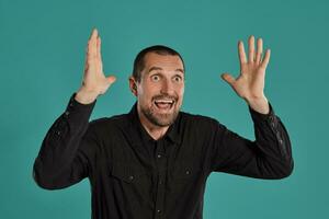 Middle-aged man with beard and mustache, wears black shirt, posing against a blue background. Sincere emotions concept. photo