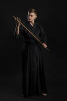 kendo gurú vistiendo en un tradicional japonés kimono es practicando marcial Arte con el shinai bambú espada en contra un negro estudio antecedentes. foto