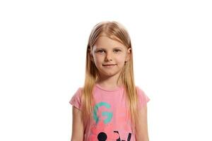 de cerca retrato de un bonito rubia pequeño niño en un rosado camiseta posando aislado en blanco antecedentes. foto