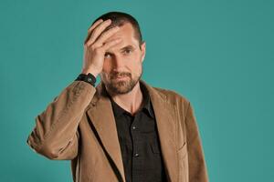 Middle-aged man with beard and mustache, wears black shirt and brown jacket posing against a blue background. Sincere emotions concept. photo