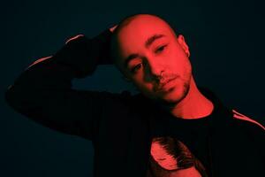 Studio shot of a young tattoed bald man posing against a colorful background. 90s style. photo