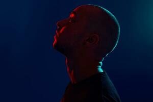 Studio shot of a young tattoed bald man posing against a blue background. 90s style. photo