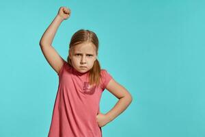 Close-up shot of beautiful blonde little girl in a pink dress posing against a blue background. photo