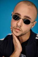 Studio shot of a young tattoed bald man posing against a blue background. 90s style. photo