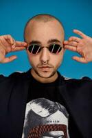 Studio shot of a young tattoed bald man posing against a blue background. 90s style. photo