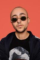 Studio shot of a young tattoed bald man posing against a pink background. 90s style. photo