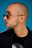 Studio shot of a young tattoed bald man posing against a blue background. 90s style. photo