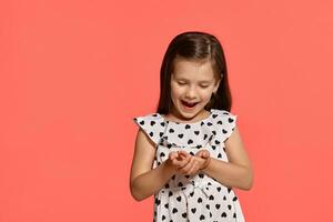 Close-up studio shot of beautiful brunette little girl posing against a pink background. photo