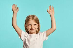 Close-up studio shot of a lovely blonde little girl in a white t-shirt posing against a blue background. photo