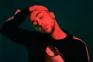 Studio shot of a young tattoed bald man posing against a colorful background. 90s style. photo