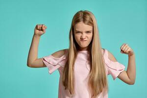 estudio retrato de un hermosa niña rubia adolescente en un rosado camiseta posando terminado un azul antecedentes. foto