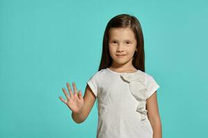 Close-up shot of a cute brunette little girl in a white blouse posing against a blue background. photo