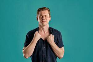 Close-up portrait of a ginger guy in navy t-shirt posing on blue background. Sincere emotions. photo