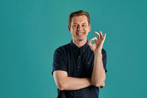 Close-up portrait of a ginger guy in navy t-shirt posing on blue background. Sincere emotions. photo