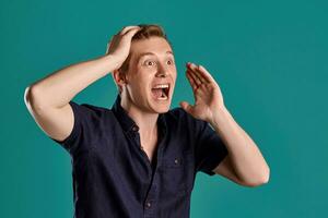 Close-up portrait of a ginger guy in navy t-shirt posing on blue background. Sincere emotions. photo