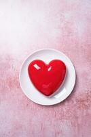 heart shaped glazed valentine cake on white plate on pink concrete background photo